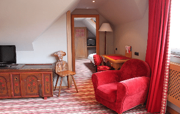 Chambre Cosy avec coin salon et fauteuil rouge à l’Hôtel Arnold